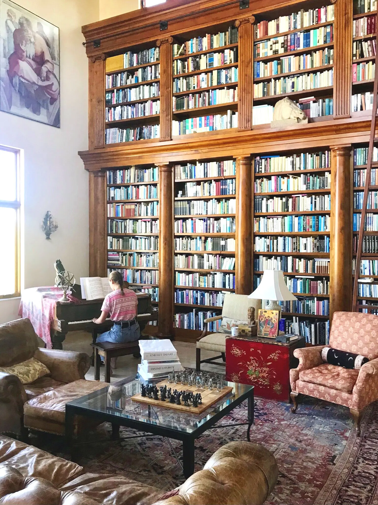 A tall wall of bookshelves in the library, with armchairs, a chess table, and a woman seated at the piano.
