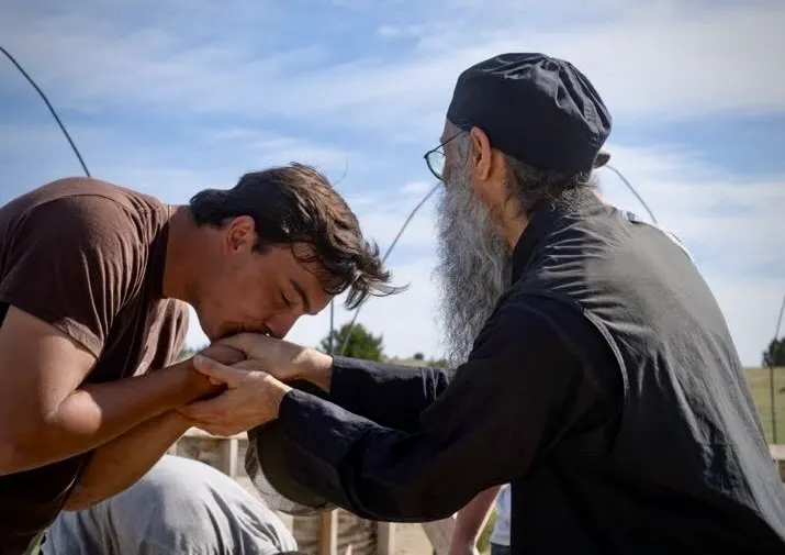 A young man bows to kiss the hand of a bearded monk, receiving his blessing.