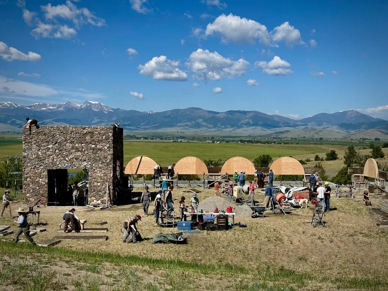The Work Week camp on the hillside: the stone entrance tower, a row of tents and crews at work, with the valley and mountains beyond.
